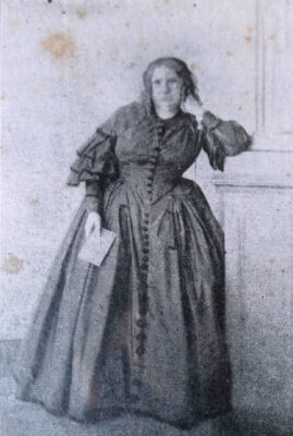 Photograph of Nísia Floresta standing with her arm propped against a wall, a pamphlet in her other hand