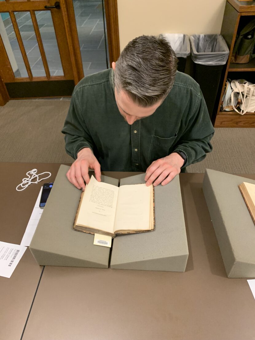 Young man reading a page of English text in a yellowed book that sits in a book rest