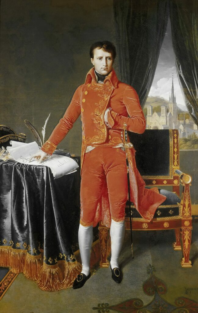 An oil portrait of Napoleon I standing in a red outfit as if mid-signing a document and staring slightly off from the viewer.